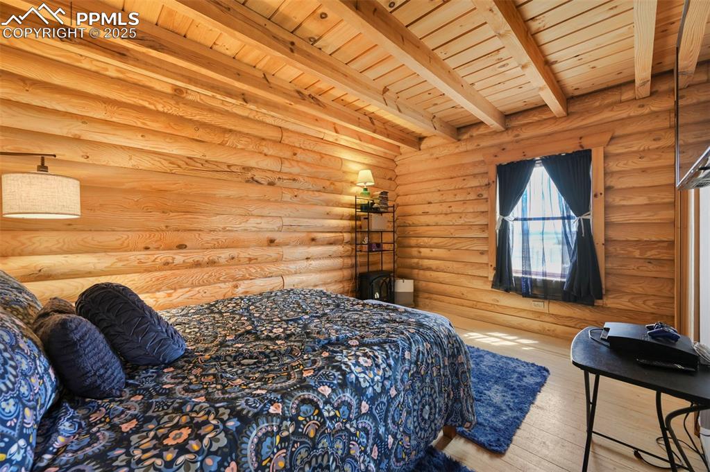 Image 10 of 35: Bedroom featuring log walls, wood-type flooring, and a wooden ceiling with 
