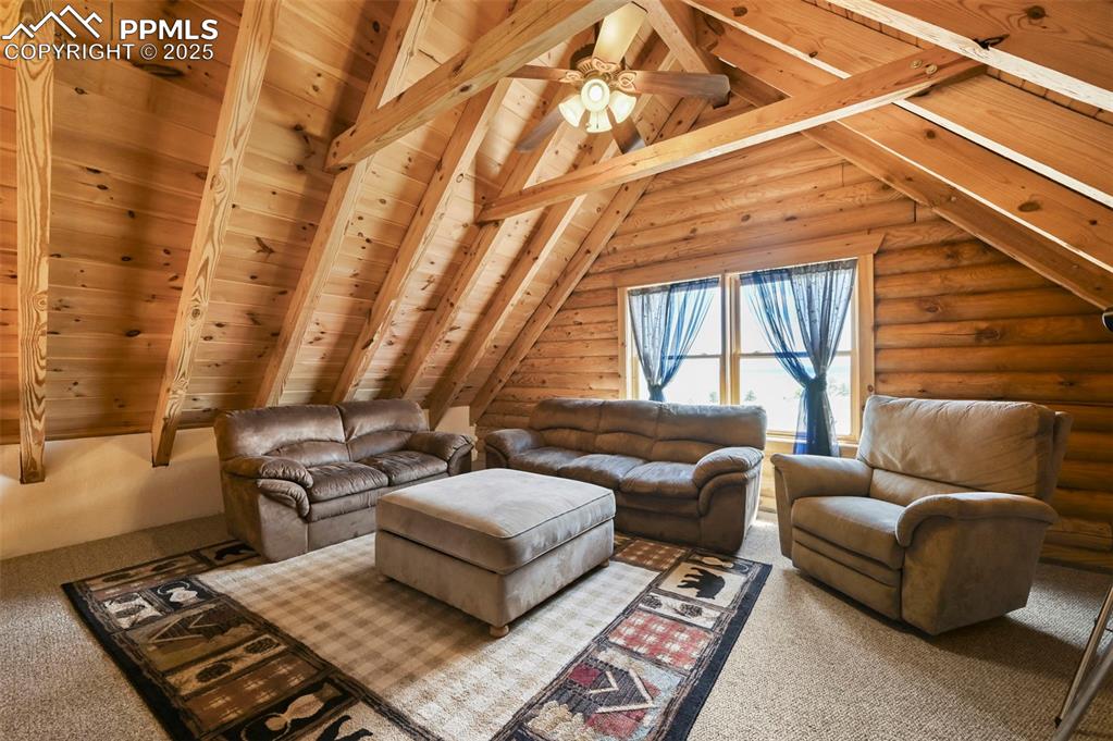 Image 16 of 35: Carpeted living area with ceiling fan, log walls, and wood ceiling