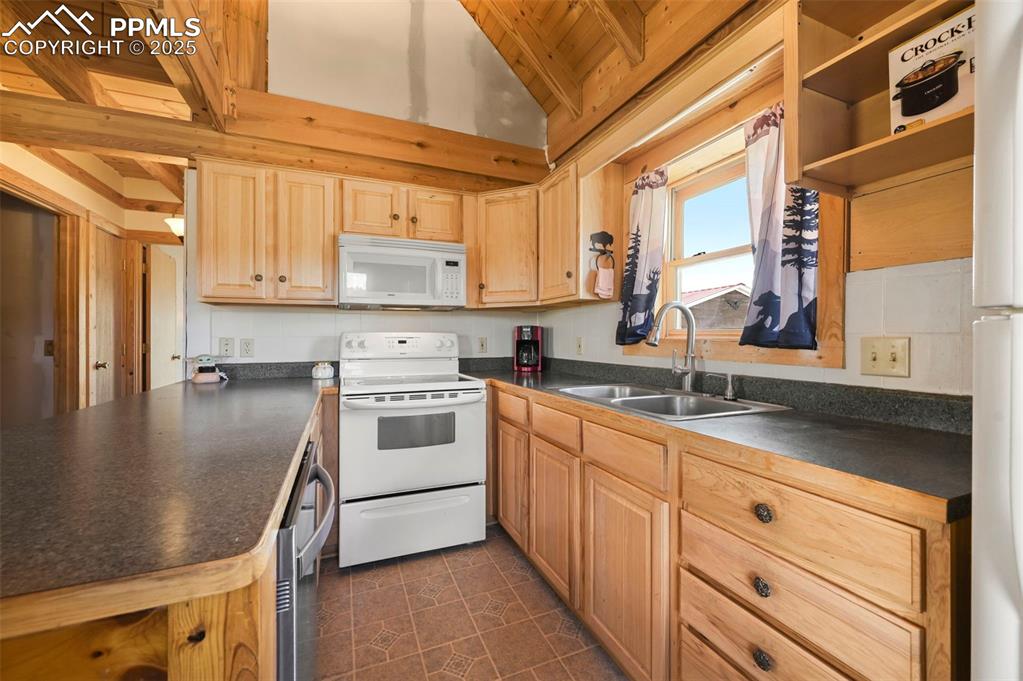 Image 7 of 35: Kitchen featuring white appliances, dark countertops, light brown cabinetry