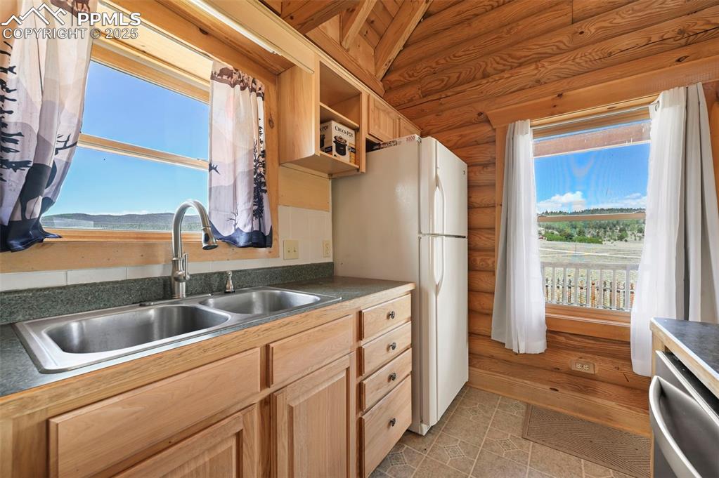 Image 8 of 35: Kitchen featuring light brown cabinetry, log walls, dishwasher, freestandin
