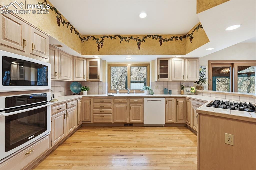 Image 15 of 49: Kitchen featuring light brown cabinetry, oven, dishwasher, light wood-style