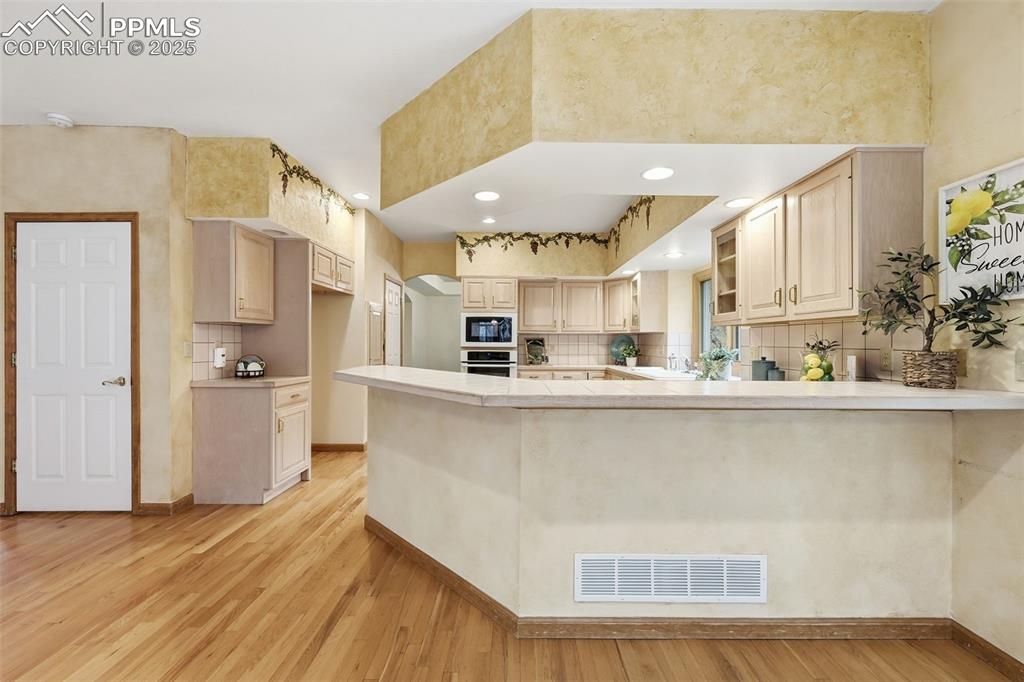 Image 16 of 49: Kitchen with light countertops, a peninsula, tasteful backsplash, wall oven