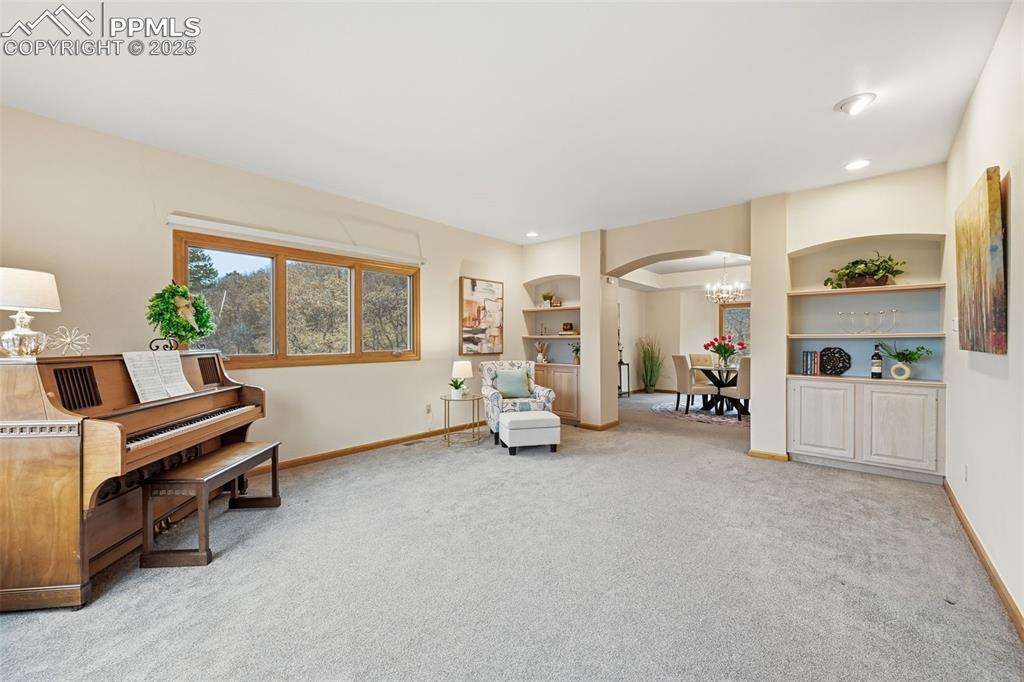 Image 19 of 49: Living area with arched walkways, a chandelier, light carpet, built in shel