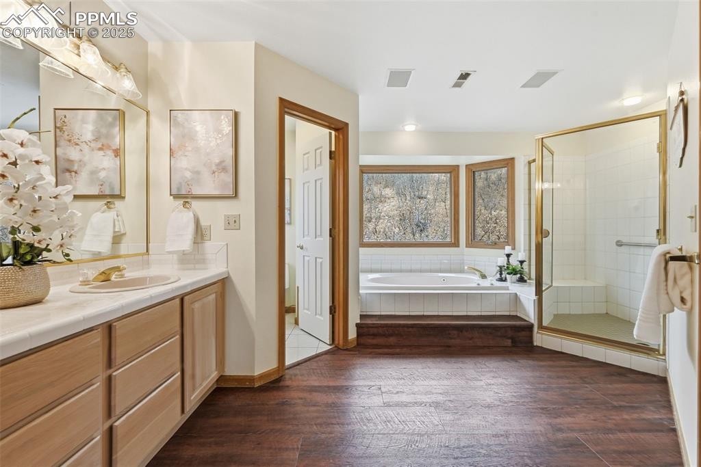 Image 27 of 49: Bathroom featuring a garden tub, a stall shower, dark wood finished floors,