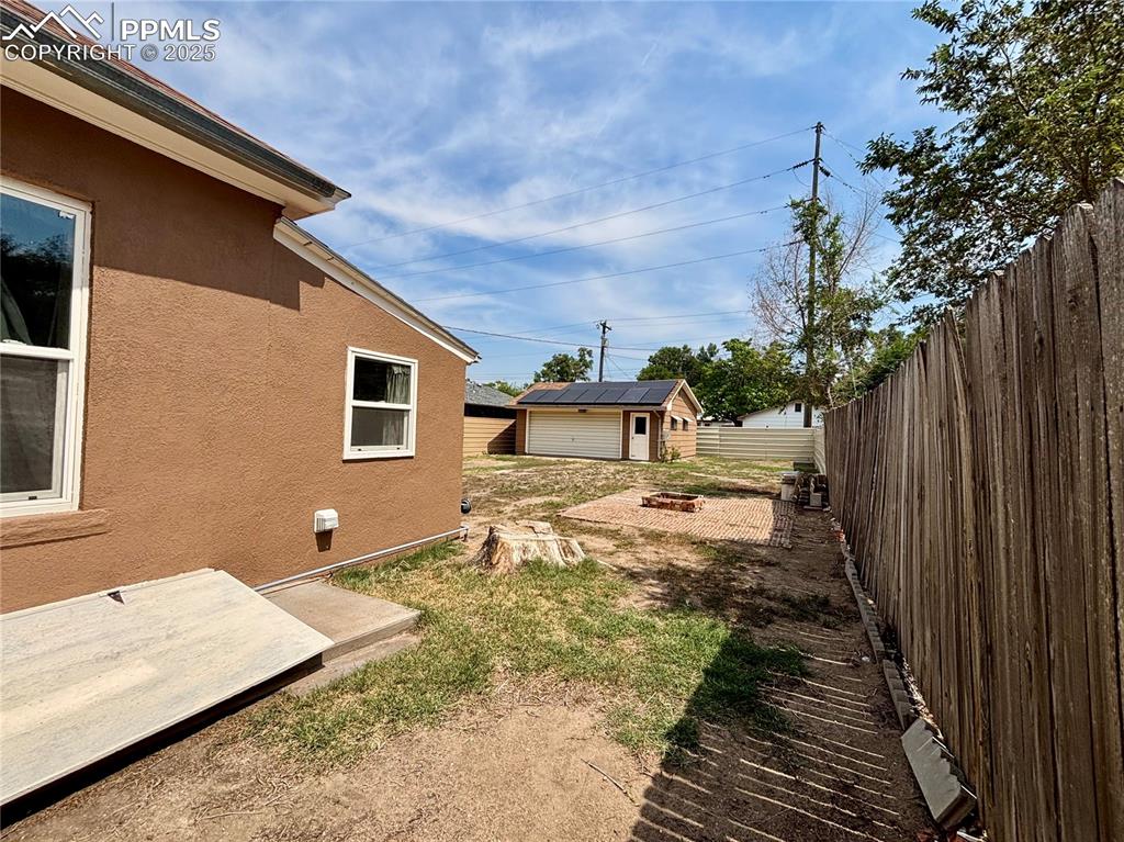Image 30 of 35: Fenced backyard with a fire pit, an outdoor structure, and a patio