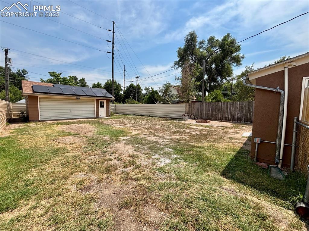 Image 31 of 35: Fenced backyard with a fire pit and a garage