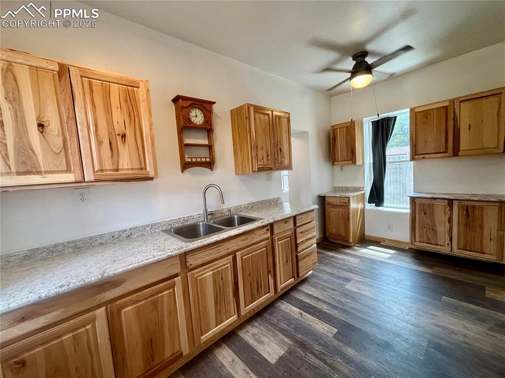 Image 8 of 35: Kitchen with a ceiling fan, dark wood finished floors, light stone counters