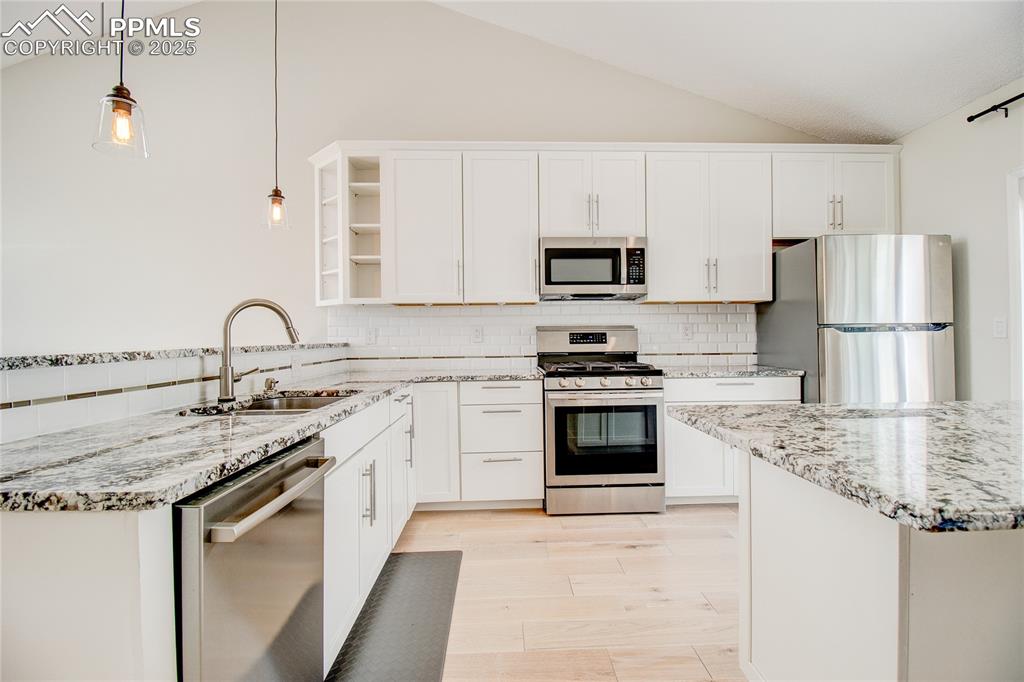 Image 10 of 32: Kitchen with appliances with stainless steel finishes, vaulted ceiling, ope