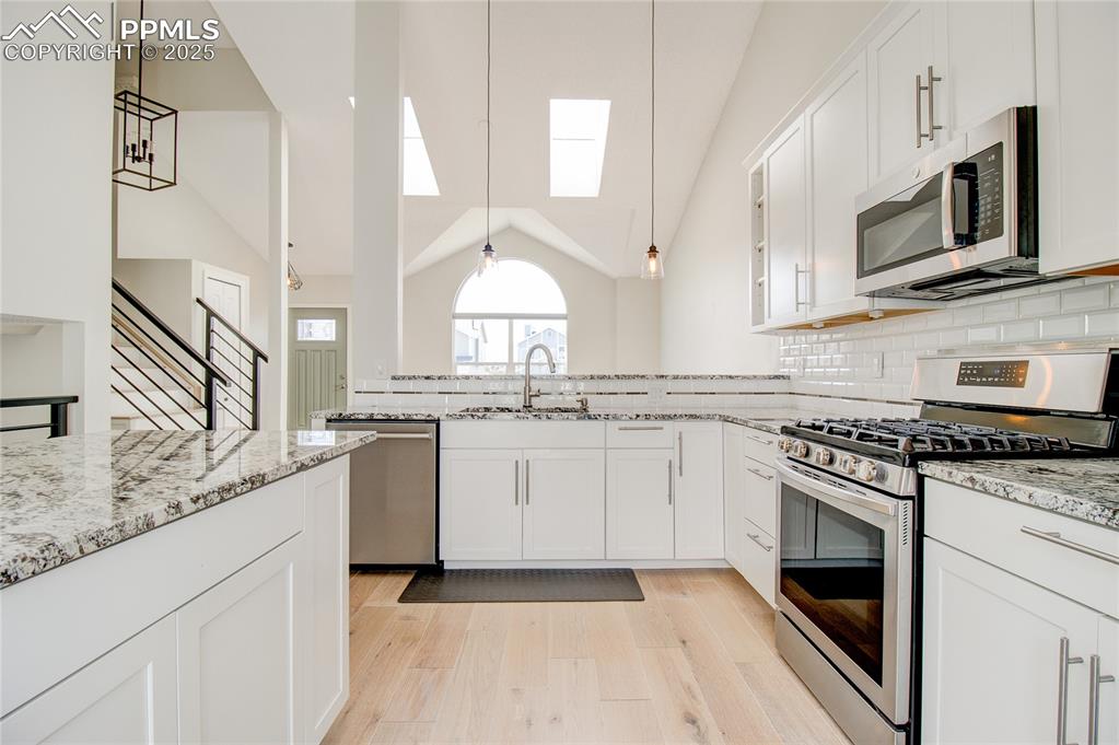 Image 11 of 32: Kitchen with appliances with stainless steel finishes, vaulted ceiling, lig