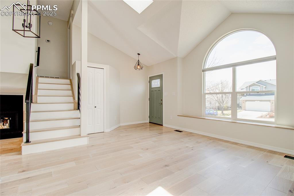 Image 14 of 32: Foyer entrance with lofted ceiling, stairs, wood finished floors, a skyligh