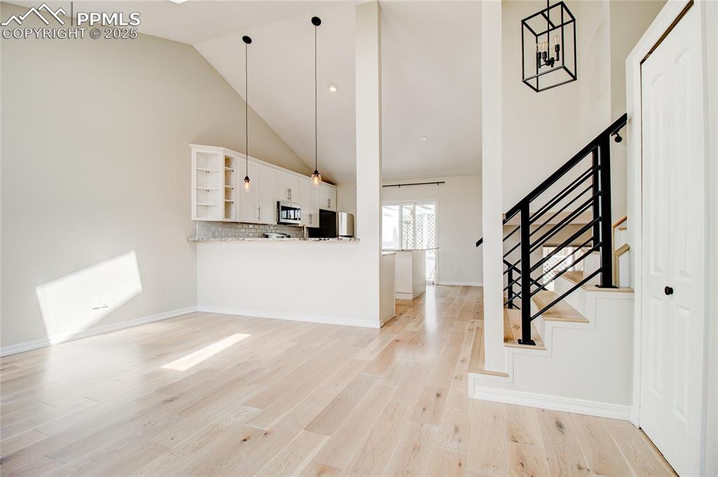 Image 2 of 32: Unfurnished living room with stairs, light wood finished floors, and high v