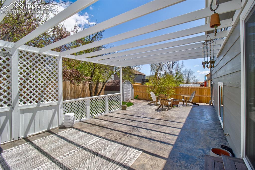 Image 29 of 32: Fenced backyard with a fire pit, a storage shed, and a pergola