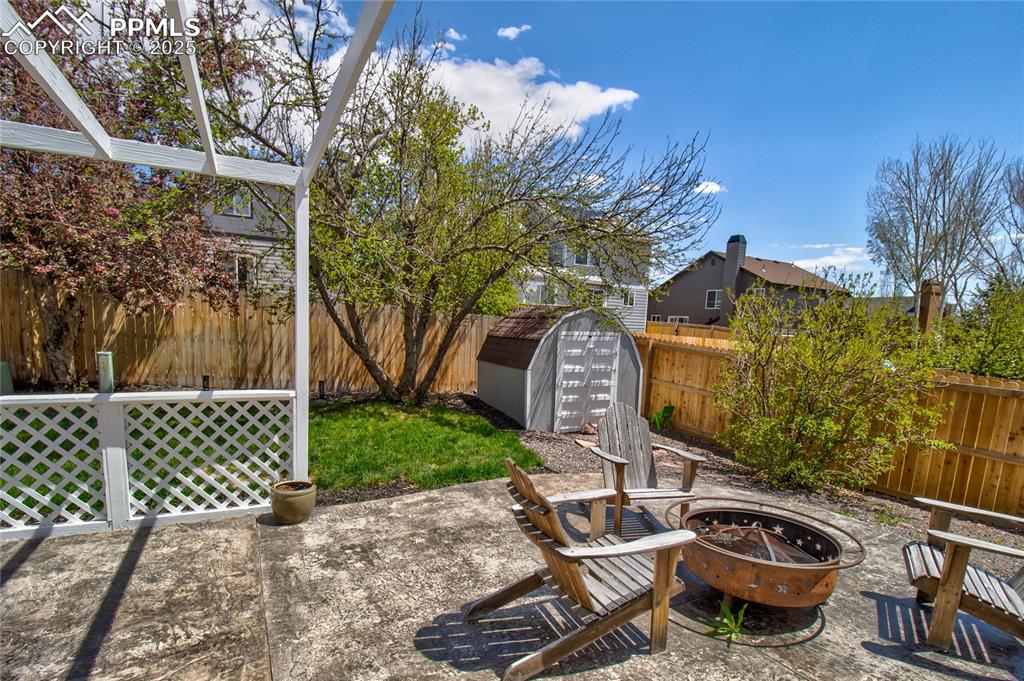 Image 32 of 32: Fenced backyard featuring a fire pit, a storage shed, and a patio area
