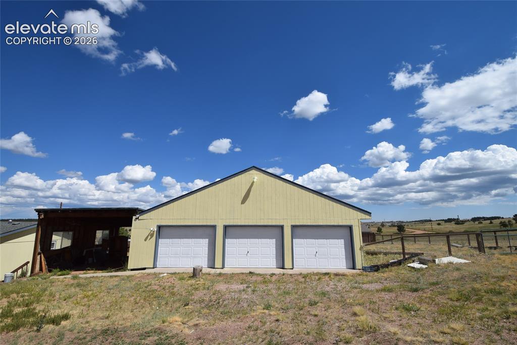 Image 3 of 48: Detached outbuilding featuring three garage doors and a covered structure