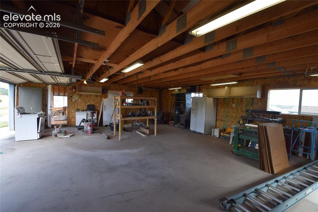 Image 44 of 48: Exposed wood beam ceiling with fluorescent lighting, concrete flooring, and