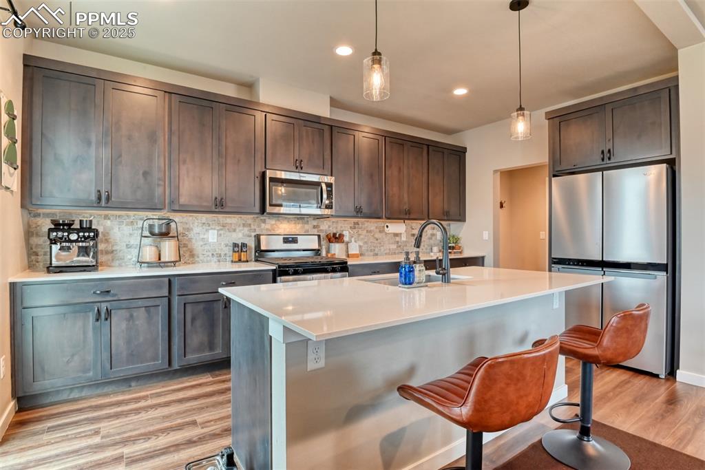 Image 45 of 50: Kitchen with tasteful backsplash, stainless steel appliances, pendant light