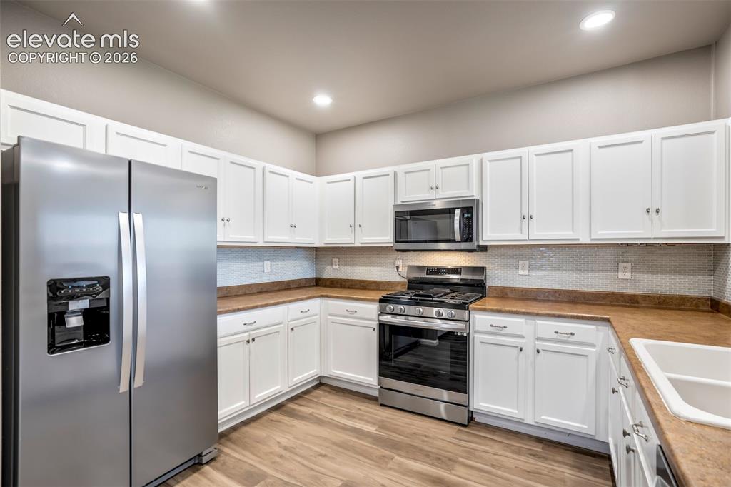 Image 11 of 50: Kitchen featuring white cabinetry, wood-finish flooring, stainless steel ap