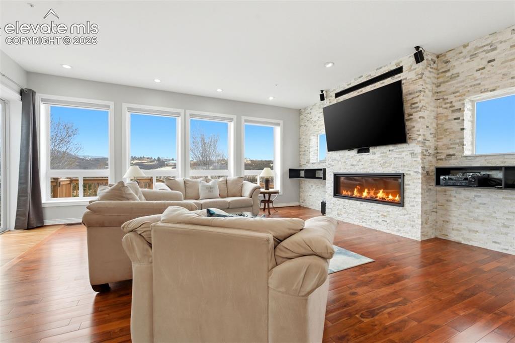 Image 14 of 46: Hardwood flooring, linear fireplace with stone surround, wall-mounted telev