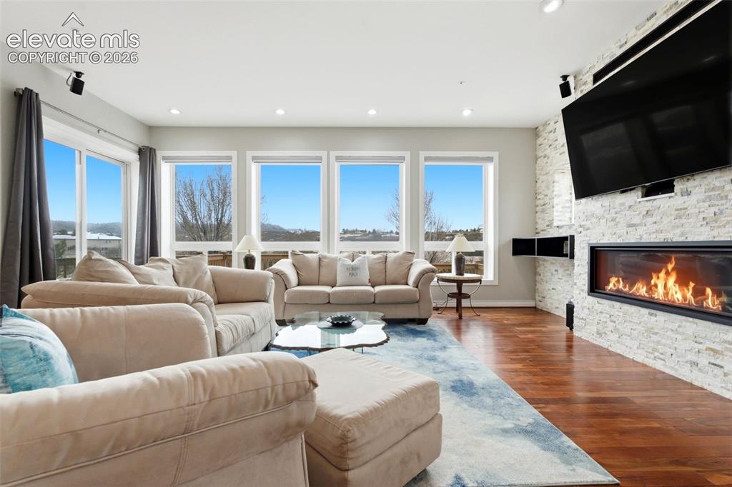 Image 16 of 46: Hardwood flooring, recessed lighting, and a linear fireplace with a stone-c