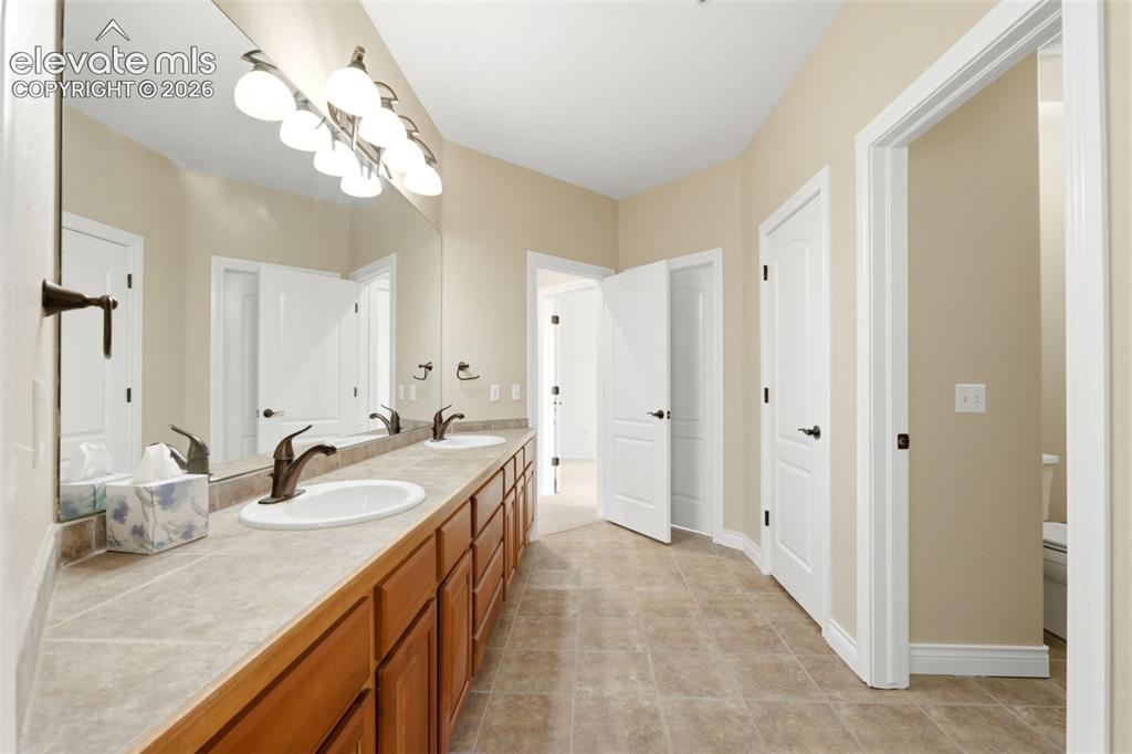 Image 39 of 46: Dual vanity with wood-finish cabinetry, integrated sinks, bronze-finish fau