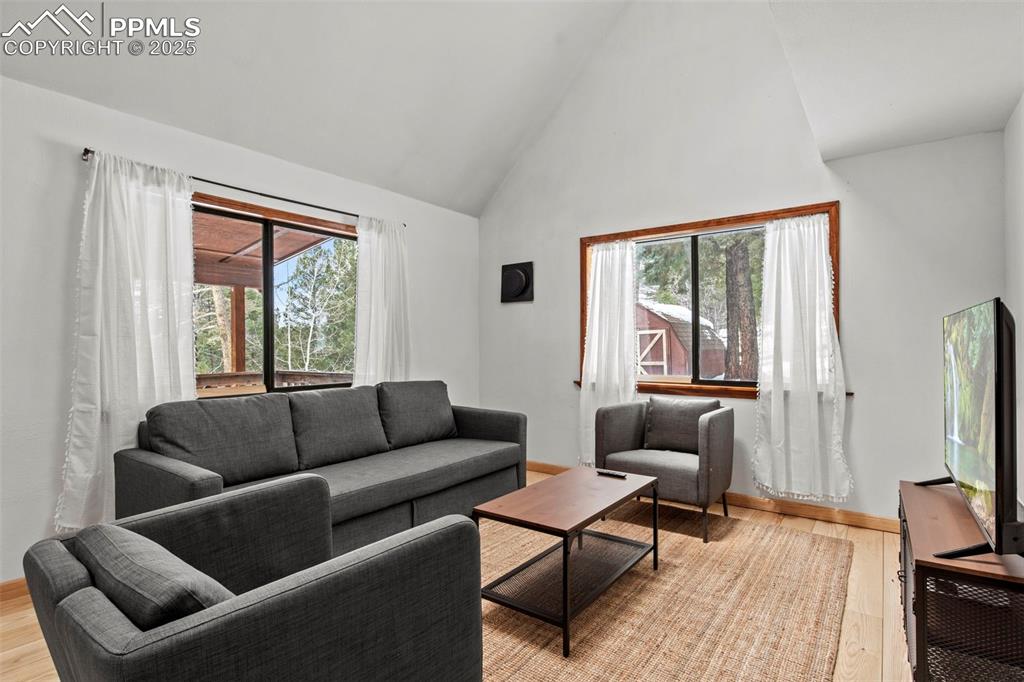 Image 11 of 50: Living area featuring light wood-style flooring and high vaulted ceiling