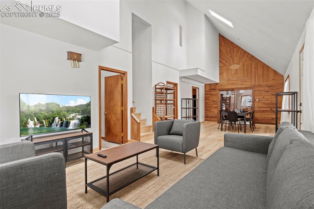 Image 13 of 50: Living area with high vaulted ceiling, wood walls, healthy amount of natura