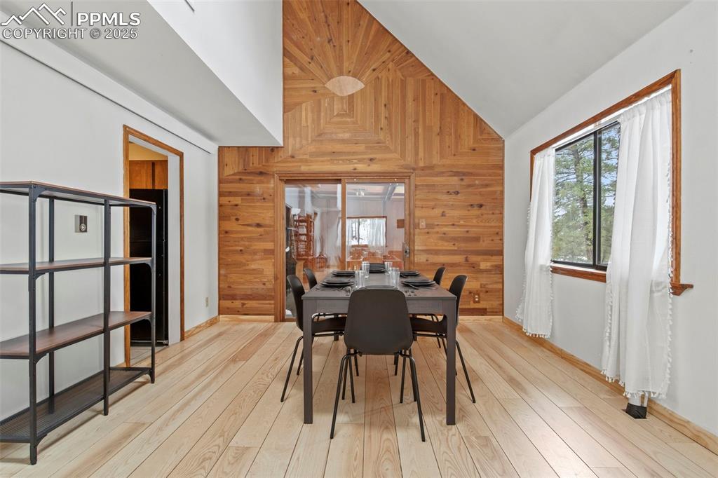 Image 14 of 50: Dining room featuring wood walls, light wood-style flooring, and lofted cei
