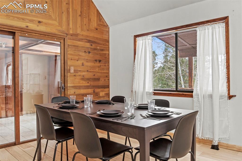 Image 15 of 50: Dining space with wood walls, wood finished floors, and vaulted ceiling
