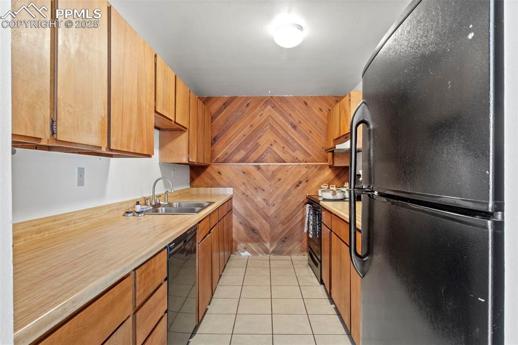Image 18 of 50: Kitchen with black appliances, wooden walls, light tile patterned floors, l