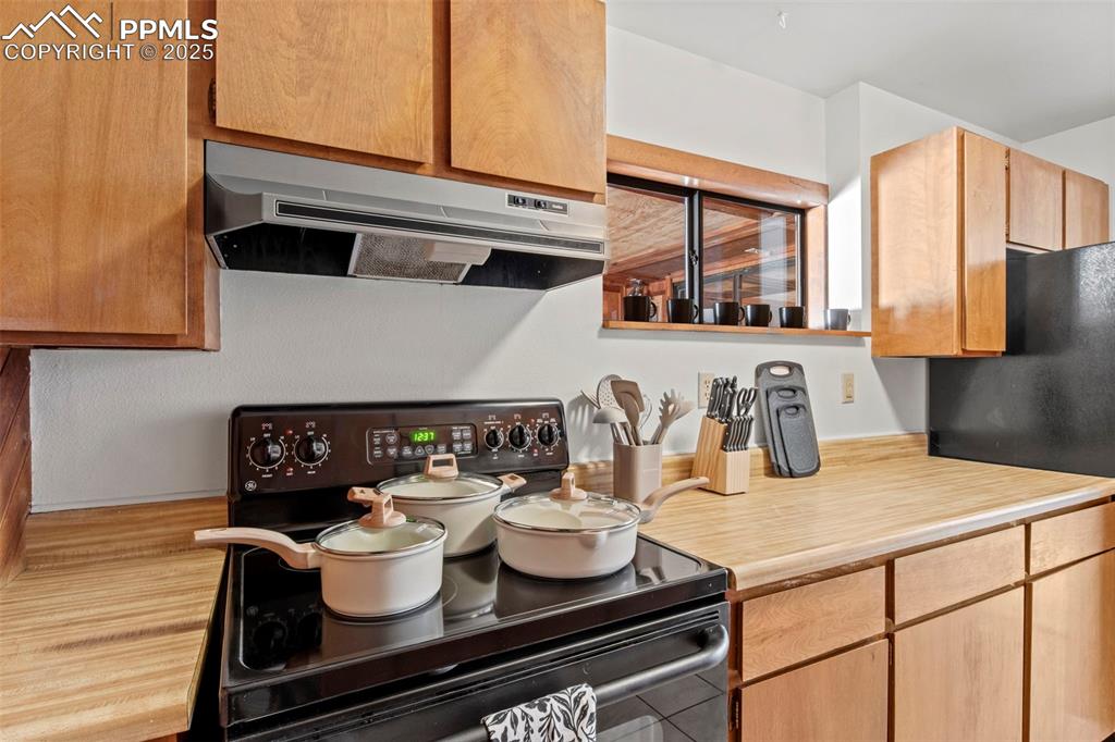 Image 21 of 50: Kitchen with black appliances, light countertops, extractor fan, and light 