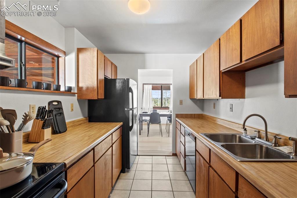 Image 22 of 50: Kitchen featuring black appliances, light tile patterned floors, brown cabi