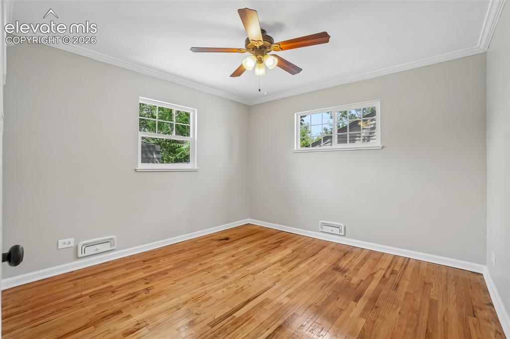 Image 13 of 34: Wood-finish flooring, two windows with white trim, ceiling fan with light f