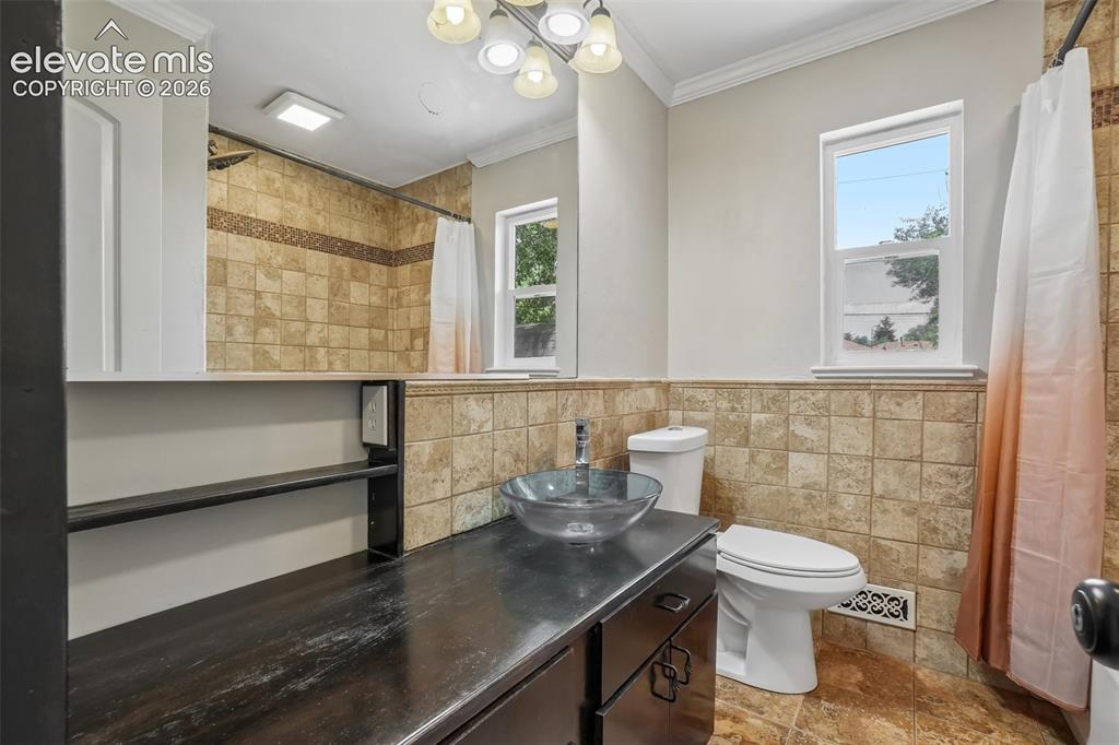 Image 15 of 34: Bathroom featuring a dark wood vanity with a glass vessel sink, tiled walls