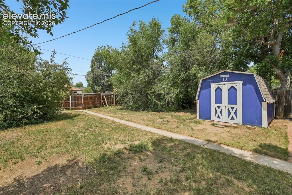 Image 26 of 34: Expansive yard with a concrete pathway, a blue barn-style shed featuring wh