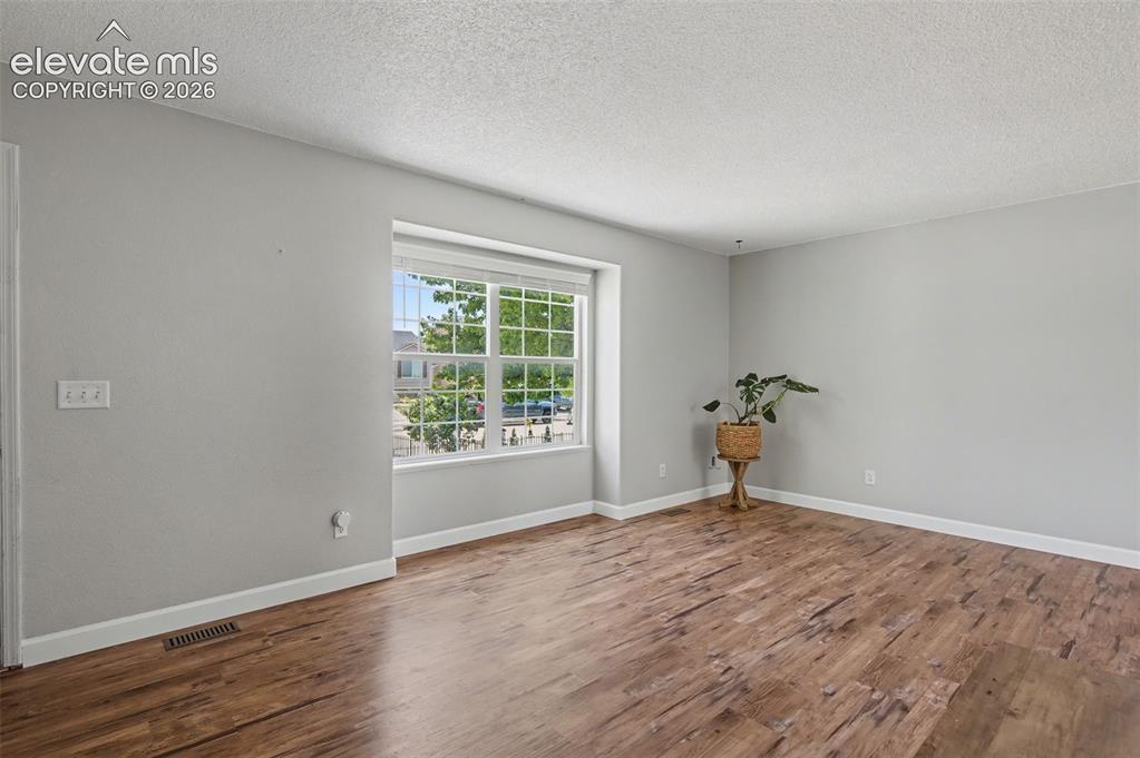 Image 5 of 37: Spacious room with wood-finish flooring, light grey walls, and white trim