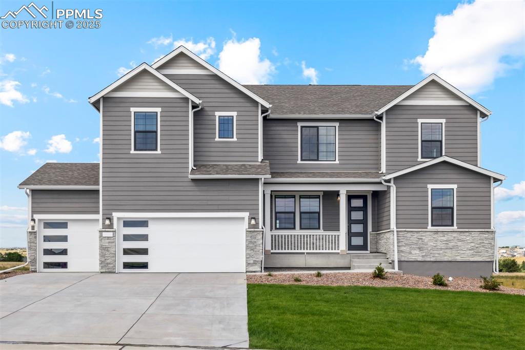 Caption: View of front of home featuring an attached garage, stone siding, driveway, a front lawn, and a porc