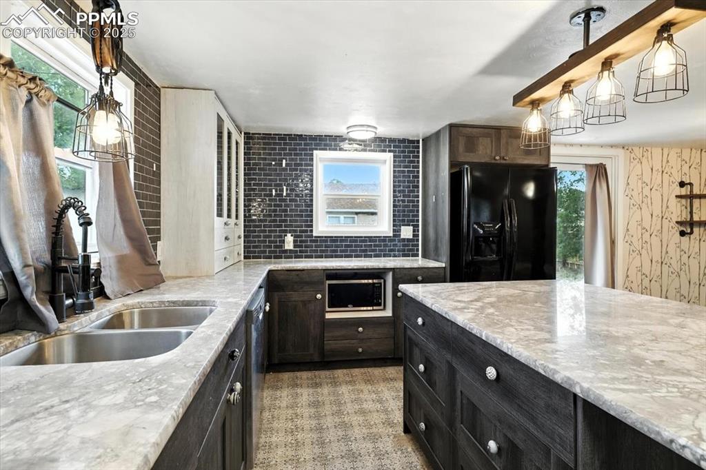 Image 11 of 30: Kitchen with black fridge, stainless steel microwave, light stone counters,