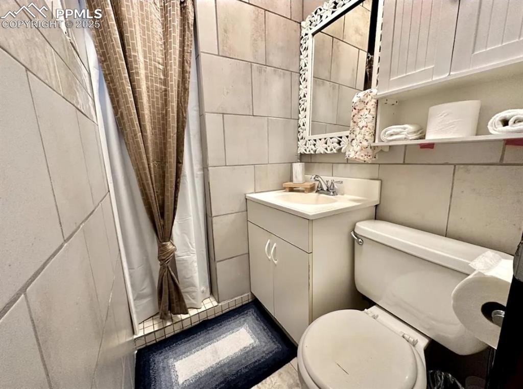 Image 14 of 16: Full bathroom featuring tile walls, a shower stall, and vanity