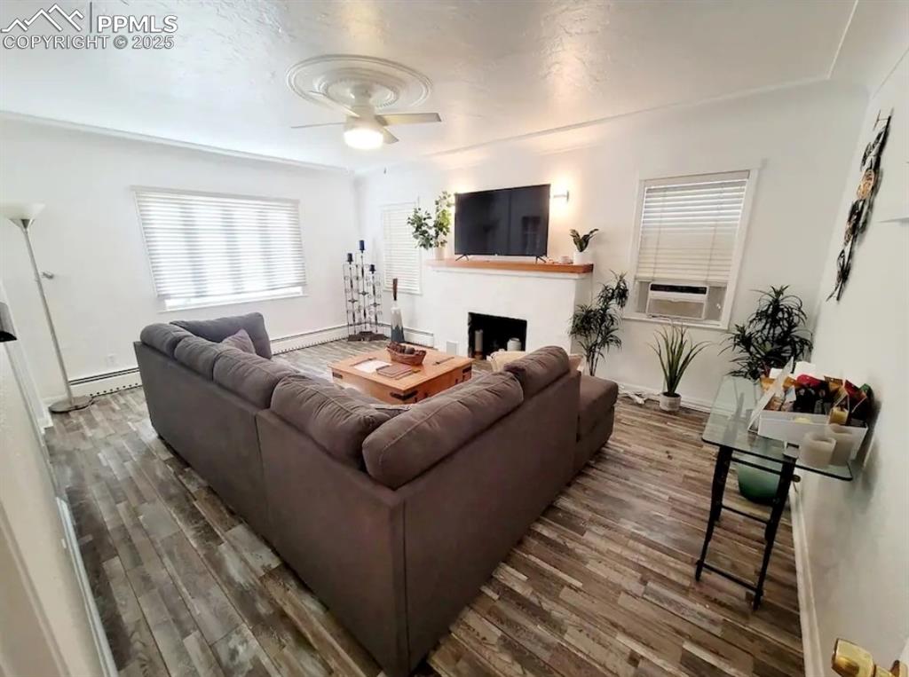 Image 5 of 16: Living area with wood finished floors, a ceiling fan, a fireplace, a basebo