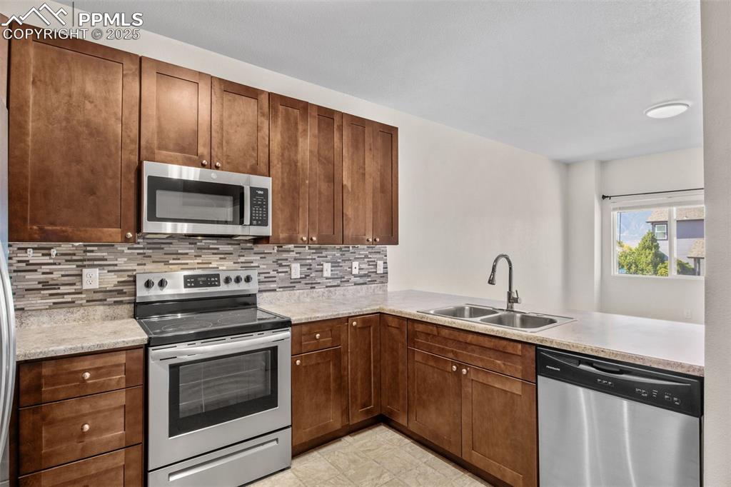 Image 14 of 41: Kitchen with stainless steel appliances, backsplash, a peninsula, and brown