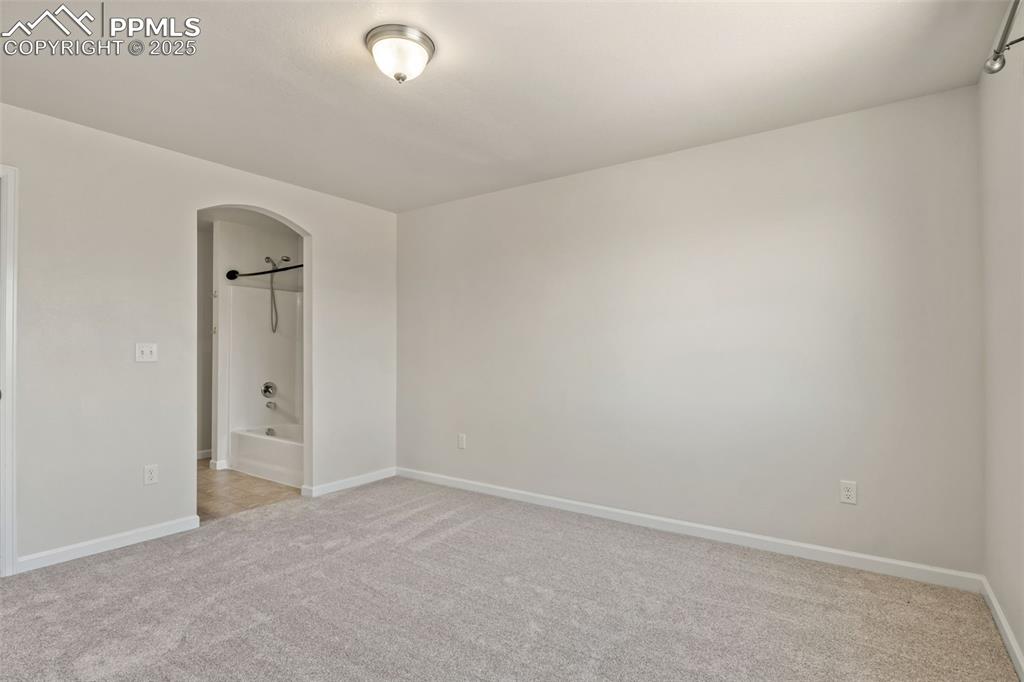 Image 23 of 41: Unfurnished bedroom with light carpet, arched walkways, and connected bathr