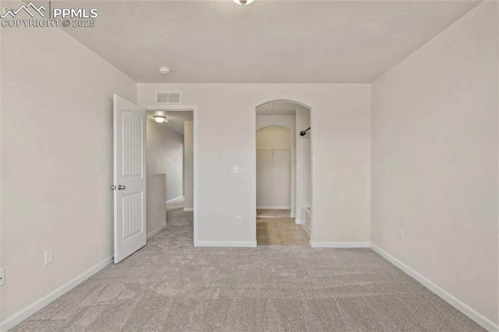 Image 26 of 41: Unfurnished bedroom with arched walkways, a walk in closet, and light carpe