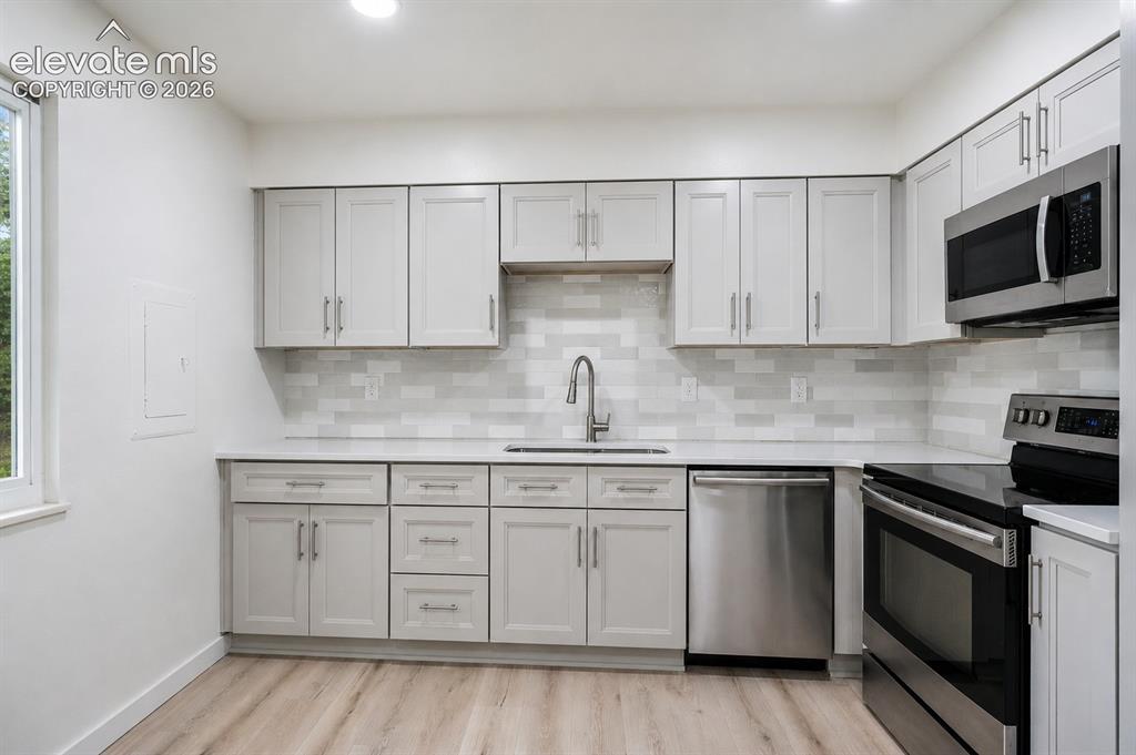 Image 10 of 47: Modern kitchen with light wood-finish flooring, white cabinetry, integrated