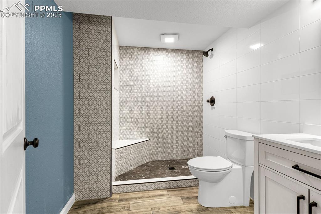 Image 25 of 38: Full bath featuring wood finished floors, tiled shower, tile walls, and van