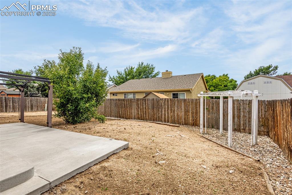 Image 28 of 38: Fenced backyard with a pergola and a patio area