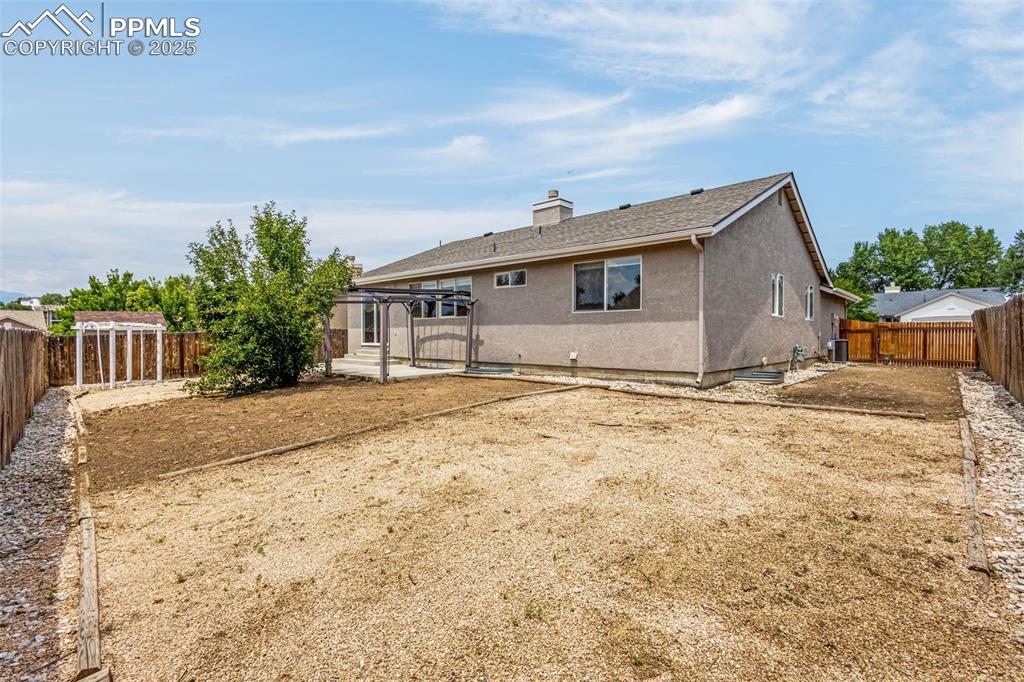 Image 29 of 38: Back of house with a fenced backyard, a chimney, stucco siding, and a shing