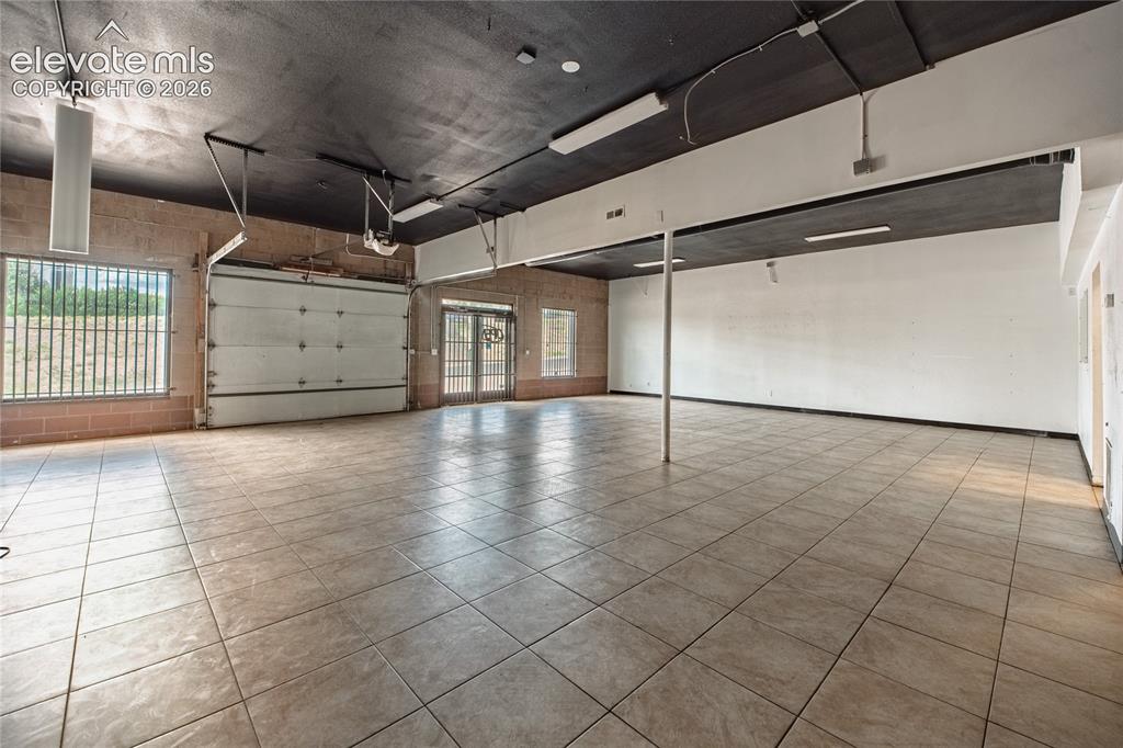 Image 11 of 50: Spacious interior featuring a roll-up garage door, tile flooring, exposed b