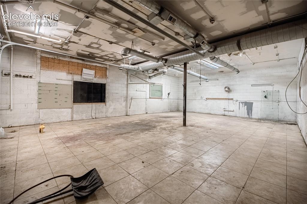 Image 18 of 50: Exposed ceiling ductwork, concrete block walls, overhead fluorescent lighti