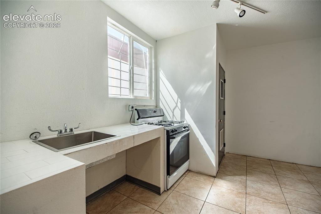 Image 27 of 50: Stainless steel sink, white wall finishes, track lighting, tiled flooring,