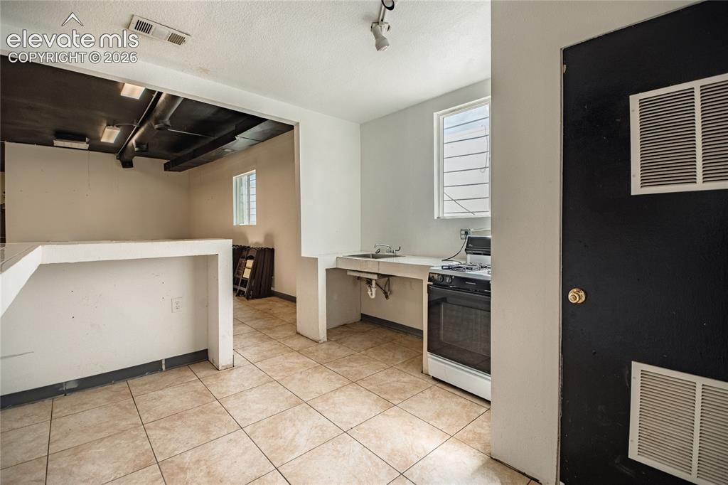 Image 28 of 50: Tile flooring, exposed ceiling ducts, built-in counter, built-in sink, and